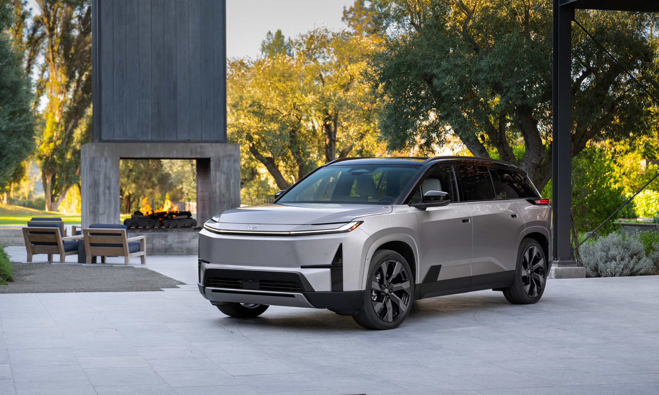 2027 Toyota Highlander Limited electric SUV in a silver two-tone finish beside an outdoor fireplace